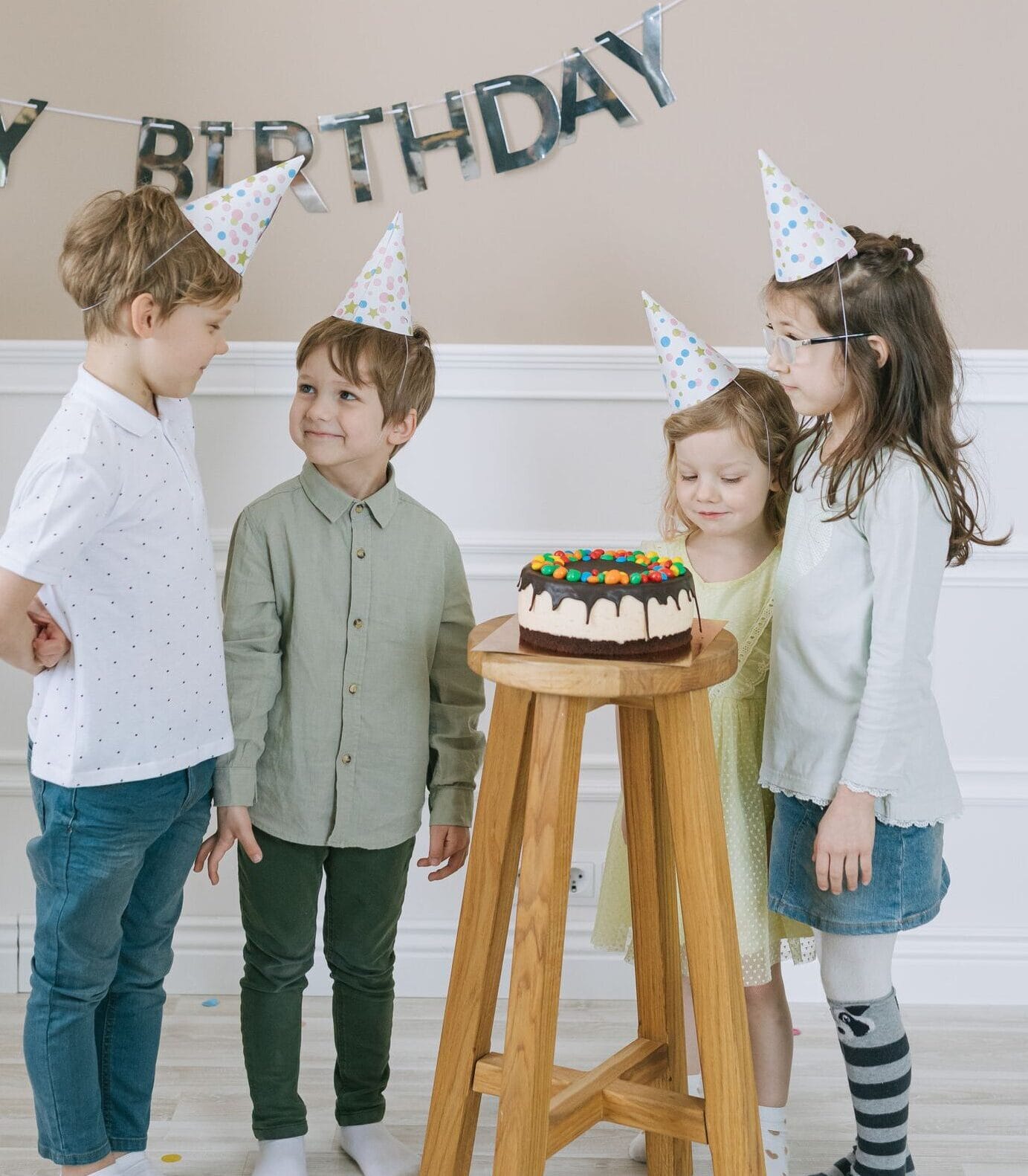 Group of kids celebrating birthday with cake and party hats, indoors.